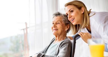 Elderly woman with wheelchair and caregiver smiling, looking outside